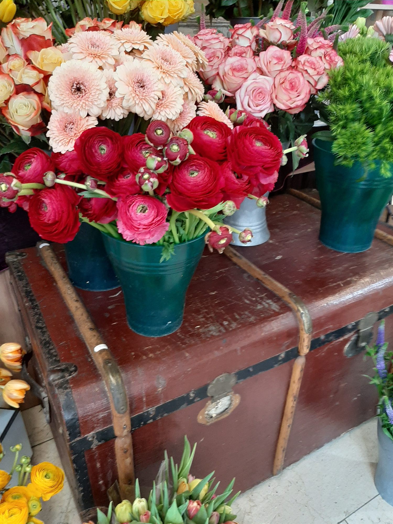 Zinkeimer mit Ranunkeln und Rosen auf einer alten Reisetruhe im Verkaufsraum